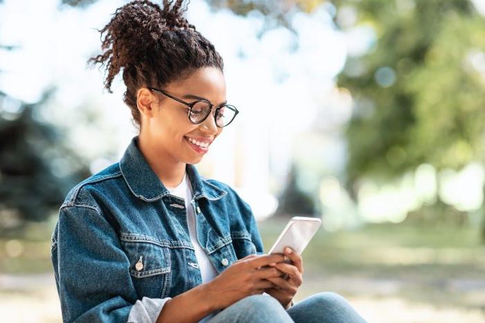 快乐的千禧一代女孩坐在户外，用智能手机使用移动应用程序.